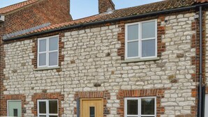 A stone building with multiple windows, a wooden door, and a brick chimney. - Seashell Cottage - UK48616 (Flamborough)