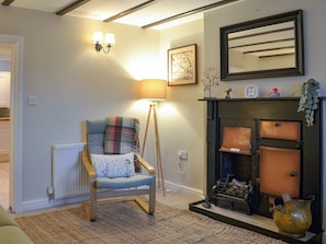 Un salón acogedor con una silla de madera, una lámpara de pie, una chimenea con un espejo encima y un radiador.