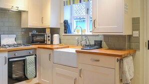 A modern kitchen with white cabinets, a gas stove, a microwave, and a toaster. - Seashell Cottage - UK48616 (Flamborough)