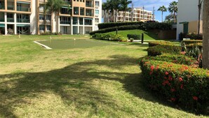 A golf course with a putting green, surrounded by well-maintained lawns and flower beds.