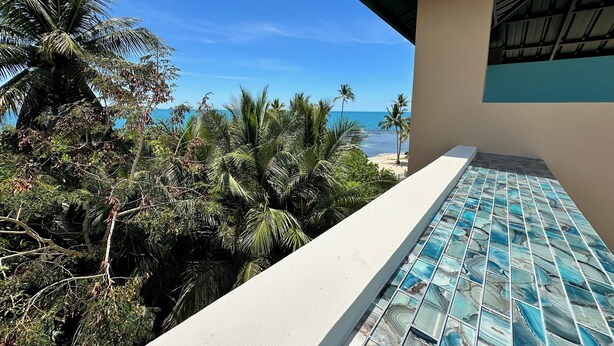 A balcony with a view of the beach and palm trees.