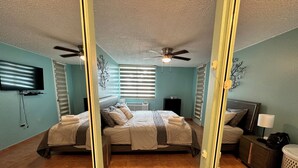 A bedroom with two beds, a ceiling fan, a TV, and a small table with a lamp.