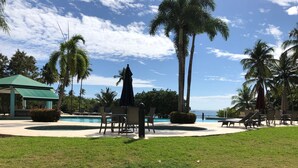 A poolside area with lounge chairs, a gazebo, and palm trees.