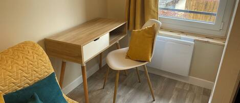 A small, cozy room with a wooden desk, a white chair, and a bed with a quilted cover.