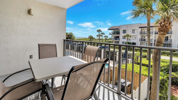 A balcony with a table and chairs, overlooking a pool and a building with multiple balconies. - Cape Winds #211 Ocean view 1 bedroom condo (Cape Canaveral)