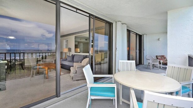 Een balkon met een glazen deur naar een woonruimte met een bank en een tafel.