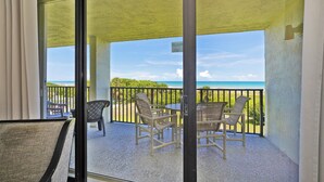 A balcony with a table and chairs, overlooking a beach with a clear sky.