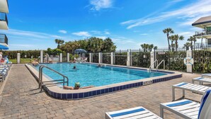 A swimming pool with a tiled edge, lounge chairs, and a fenced area with palm trees.
