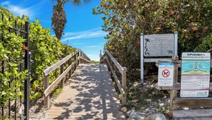 A wooden boardwalk leading to a beach area with signs and a palm tree.