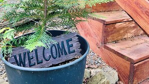 Un árbol navideño en maceta con un cartel que dice 'WELCOME', colocado en una maceta negra frente a unos escalones de madera.