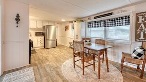 Una cocina moderna con armarios blancos, un refrigerador de acero inoxidable y un comedor con mesa y sillas de madera.