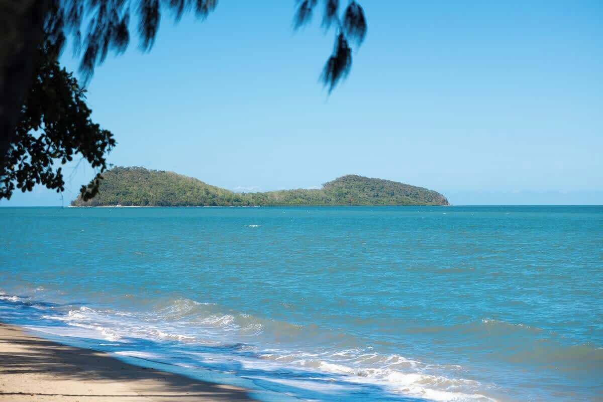 A beach with clear blue water, a sandy shore, and a distant island.