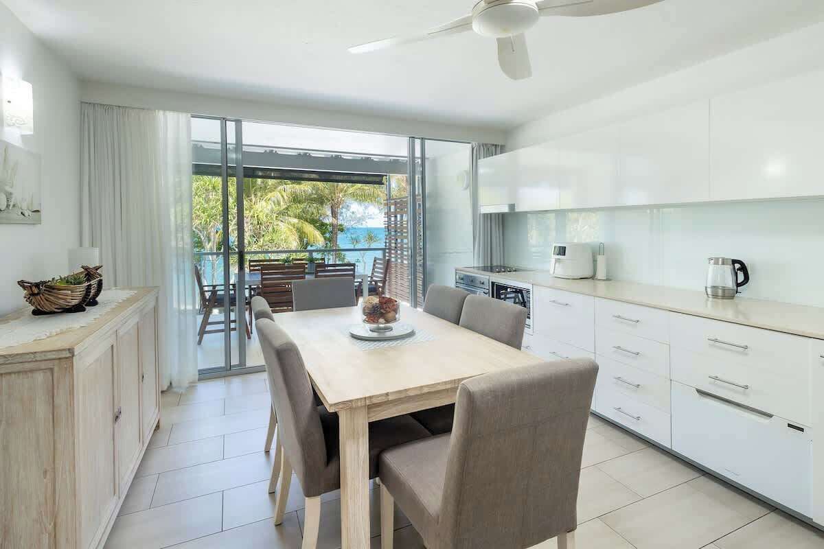 A modern kitchen with a dining area, large windows, and a view of the outdoors.