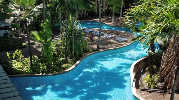 Ein Poolbereich mit geschwungenem Design, umgeben von Palmen und Liegestühlen.