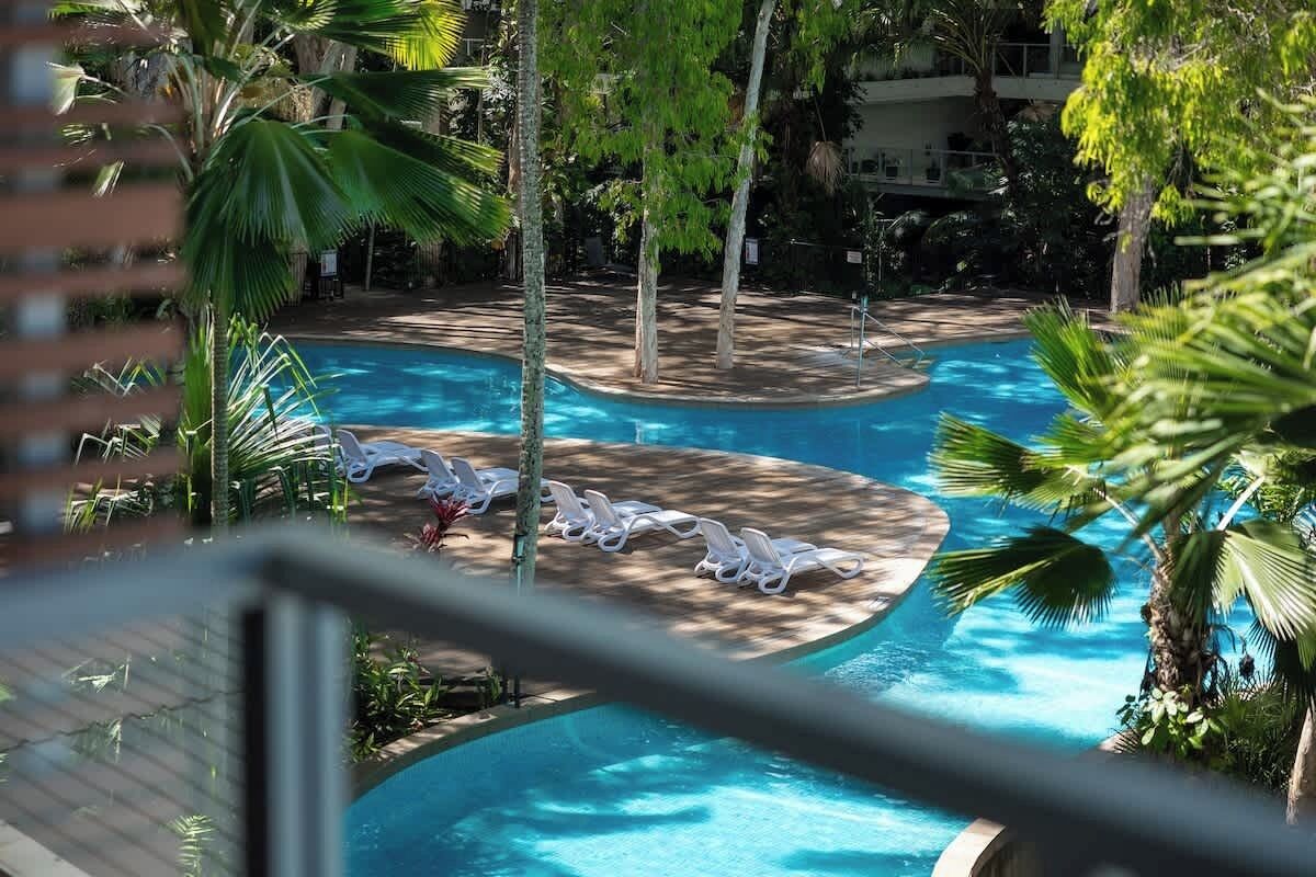 Ein Pool mit Liegestühlen, umgeben von Palmen und viel Grün.