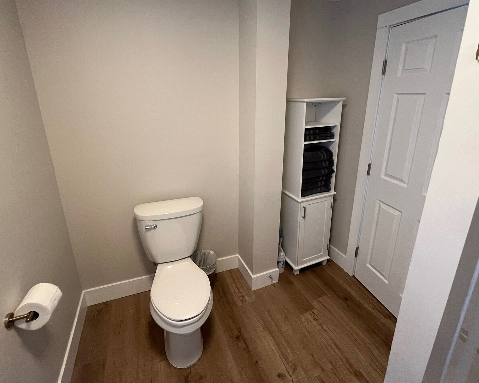 Un baño pequeño con un inodoro blanco, un armario blanco con estantes y una puerta blanca.