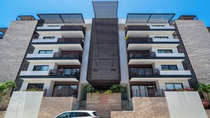A multi-story building with balconies, a central vertical structure, and a car parked in front. - Modern PH with 2 Br & Pool at Arena 509 (Playa del Carmen)