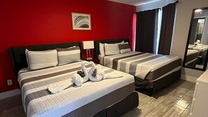 A hotel room with two beds, a ceiling fan, a red wall, and a mirror.