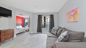A modern bedroom with a bed, a wooden dresser, a TV, and a window with curtains.