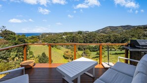 Une terrasse offrant une vue sur un paysage côtier, avec des collines et une étendue d’eau.