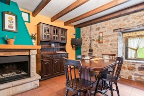 A rustic kitchen with a stone wall, wooden cabinets, a fireplace, and a dining table with chairs.