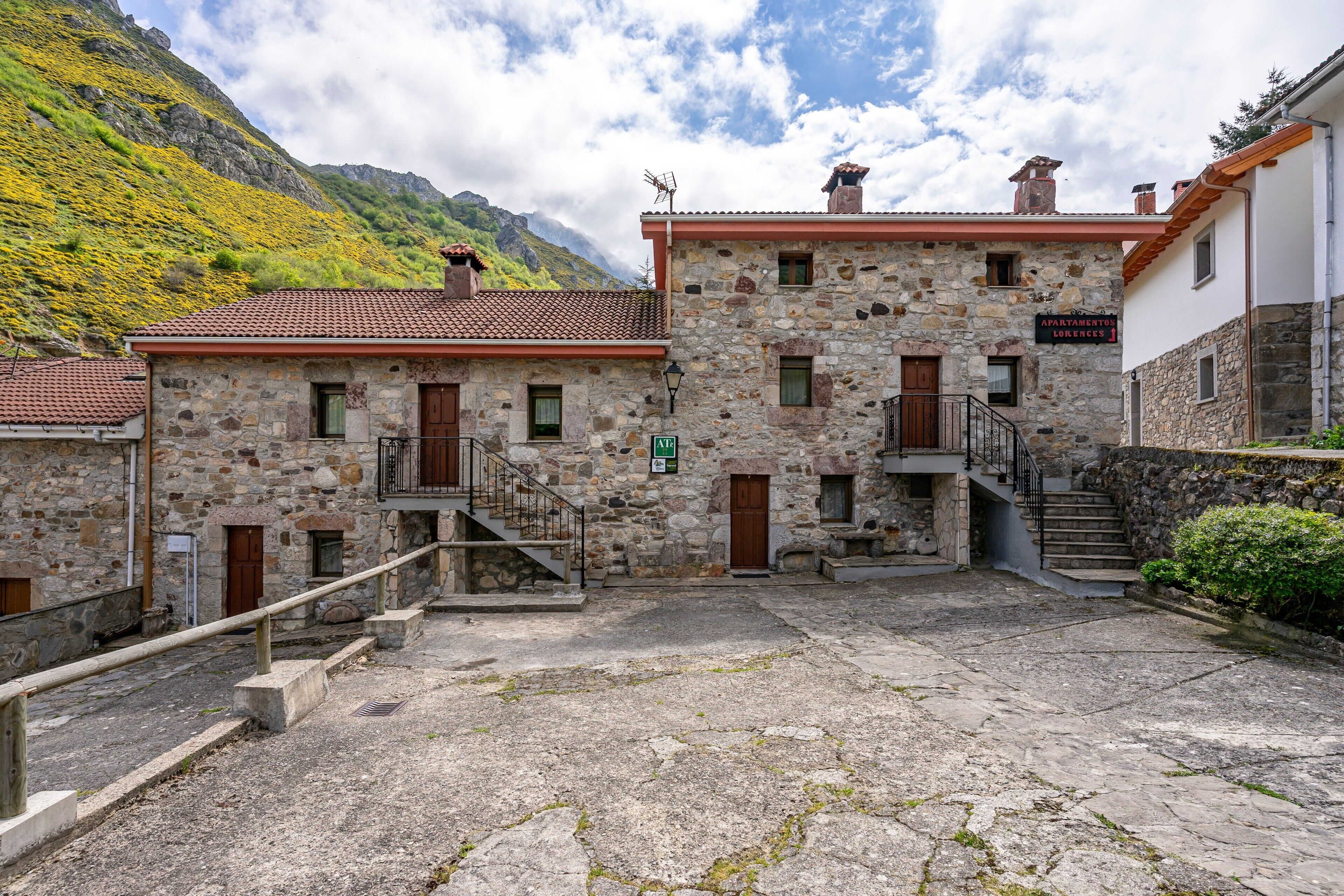 Ein Steinhaus mit rotem Ziegeldach, zahlreichen Fenstern und einer Treppe, die zu einer oberen Ebene führt.