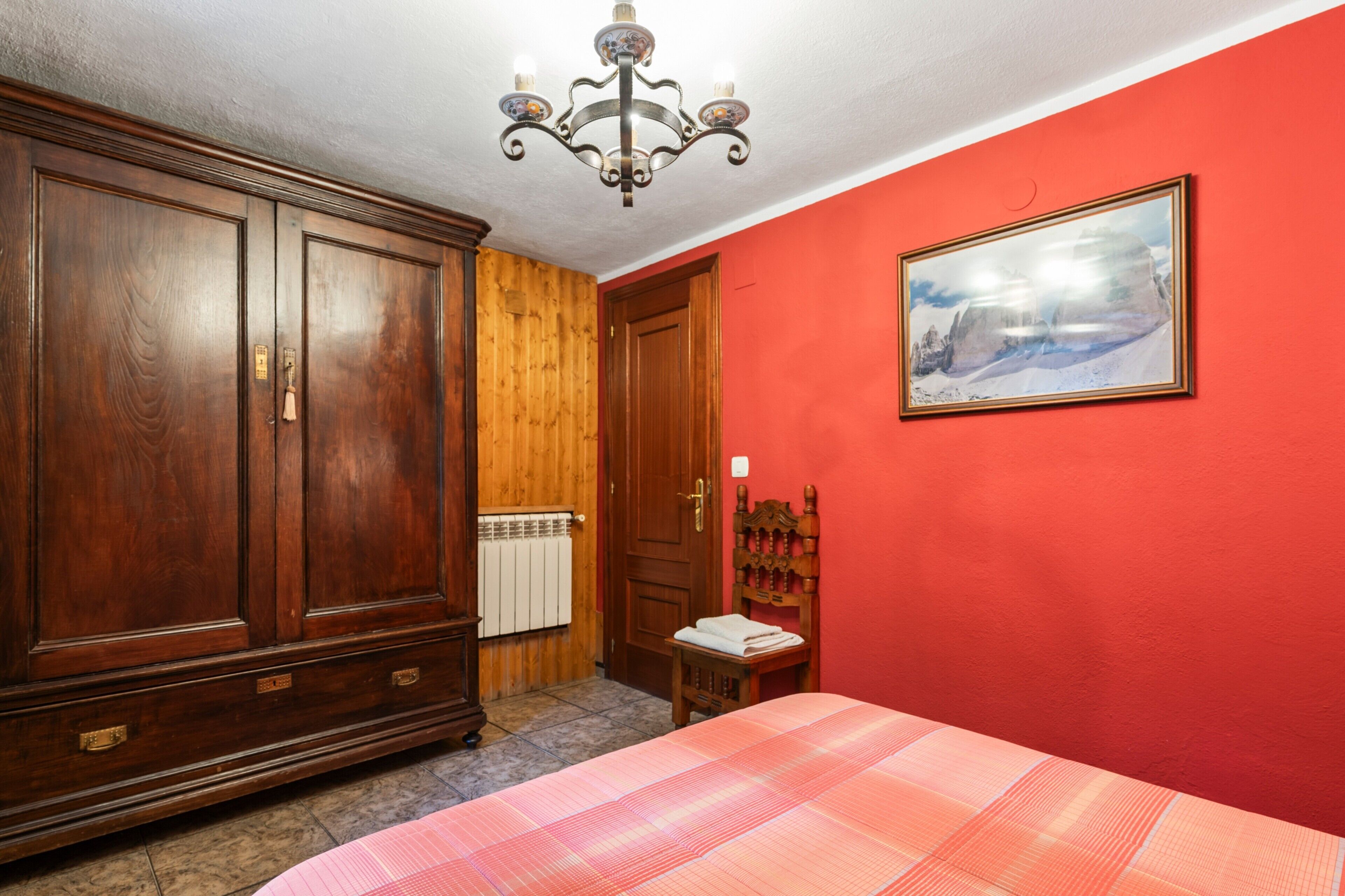 Una habitación con un armario grande, una cama con cubrecama a cuadros, una puerta de madera y un cuadro en la pared.