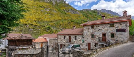 A stone building with a car parked in front, a stone wall, and a mountain in the background.