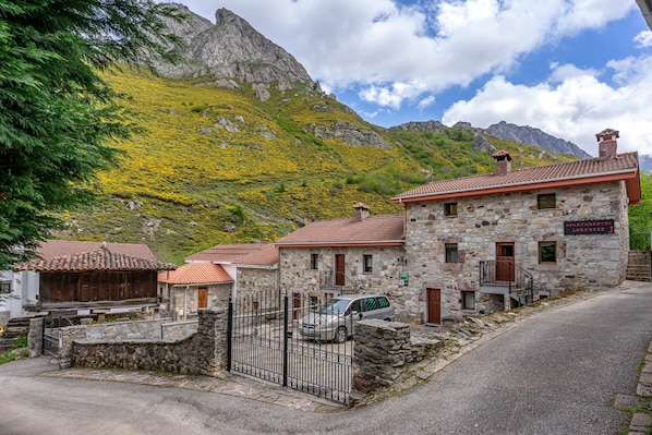 A stone building with a car parked in front, a stone wall, and a mountain in the background.