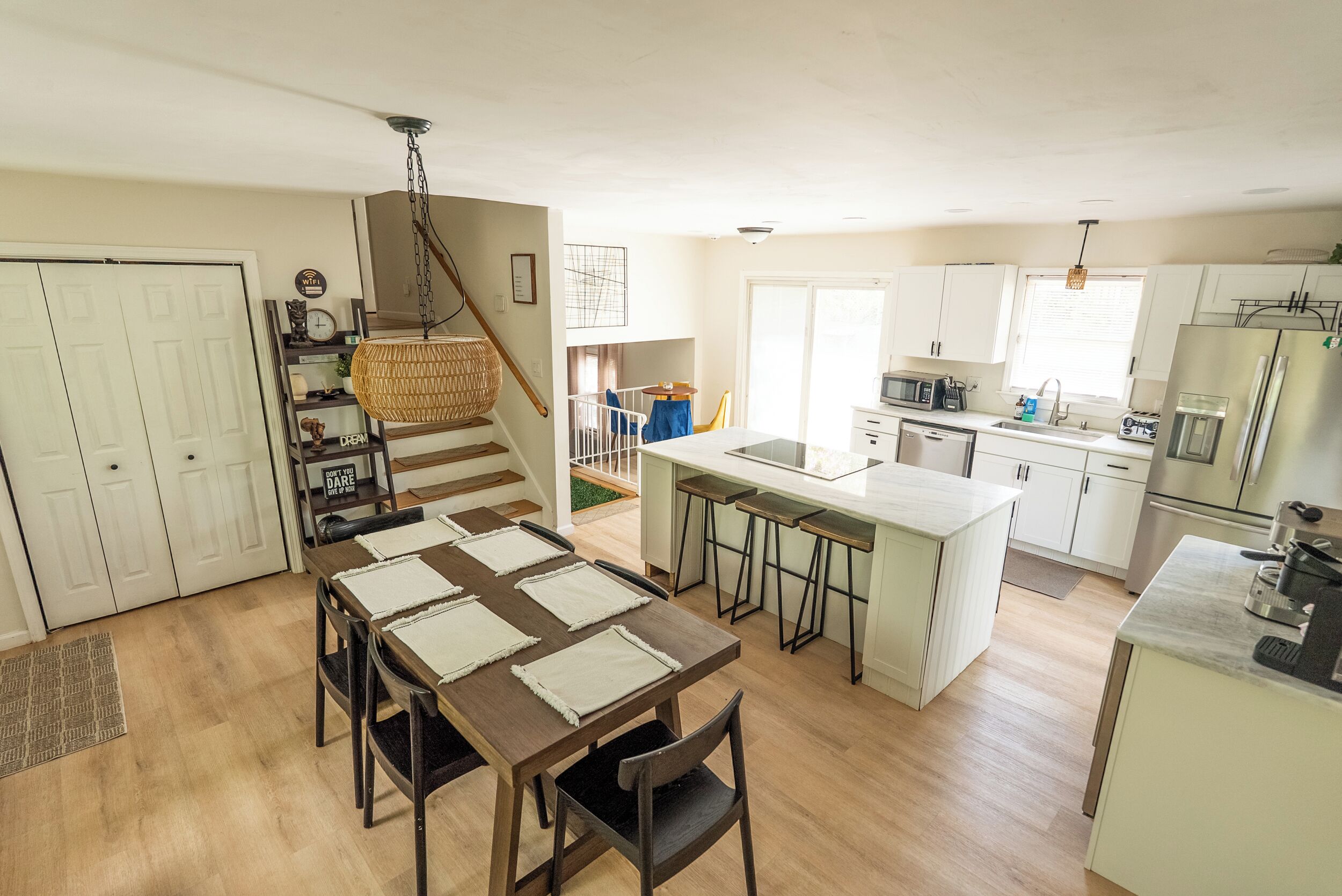 A modern kitchen with white cabinets, a central island, and a dining area with a wooden table and chairs.