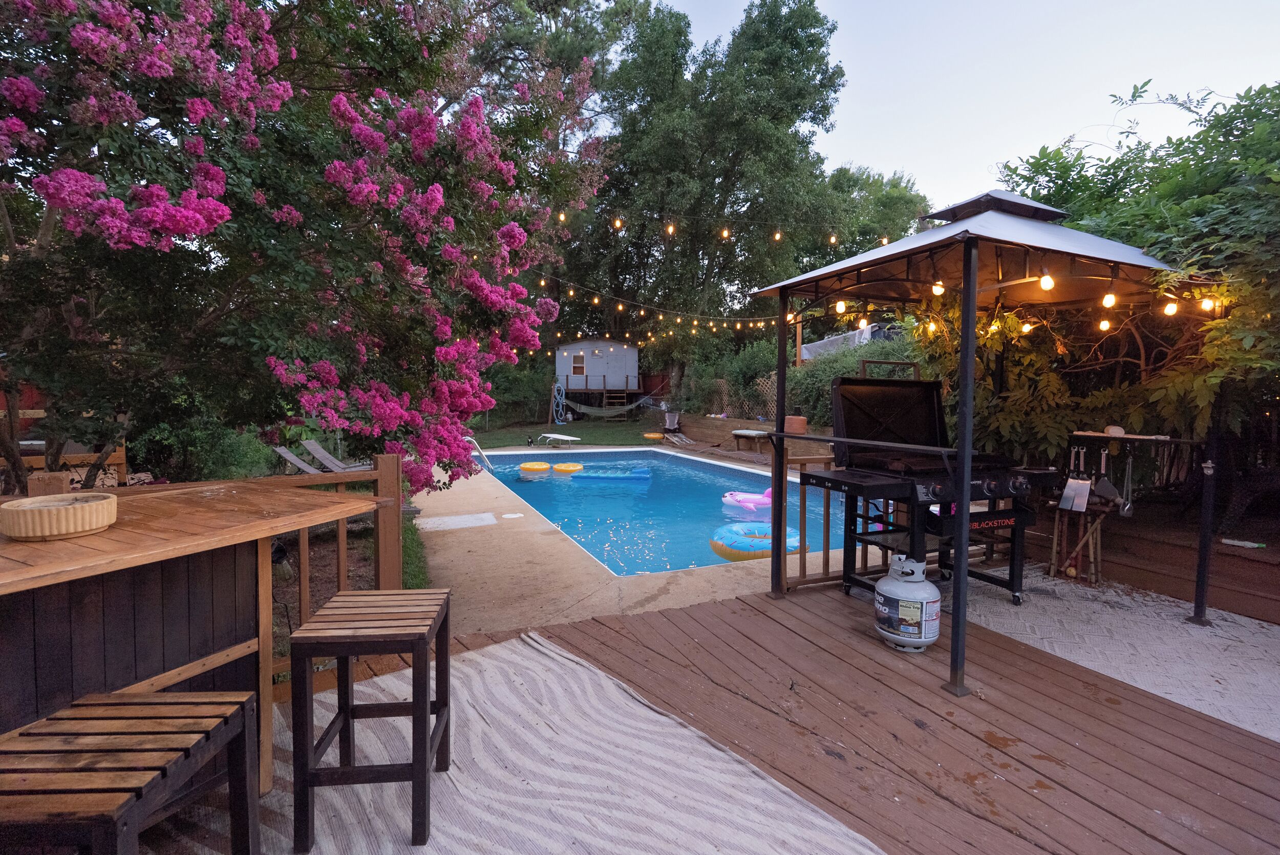 A backyard with a wooden deck, a swimming pool, a barbecue area, and a covered seating area.