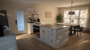 A modern kitchen with white cabinetry, a built-in oven, and a dining area with a table and chairs.