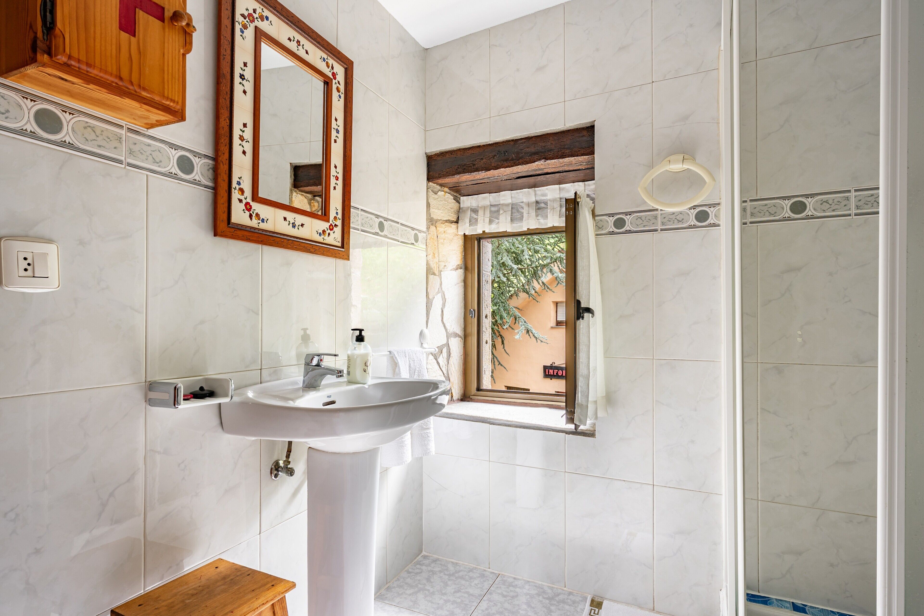 Un baño con lavamanos, espejo, mueble de madera y ventana con vistas.