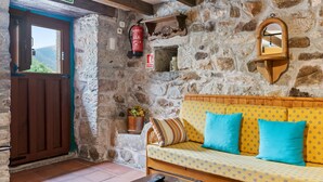A stone-walled room with a wooden door labeled 'SALIDA,' a wooden bench with cushions, a fire extinguisher, and a small shelf with a mirror.