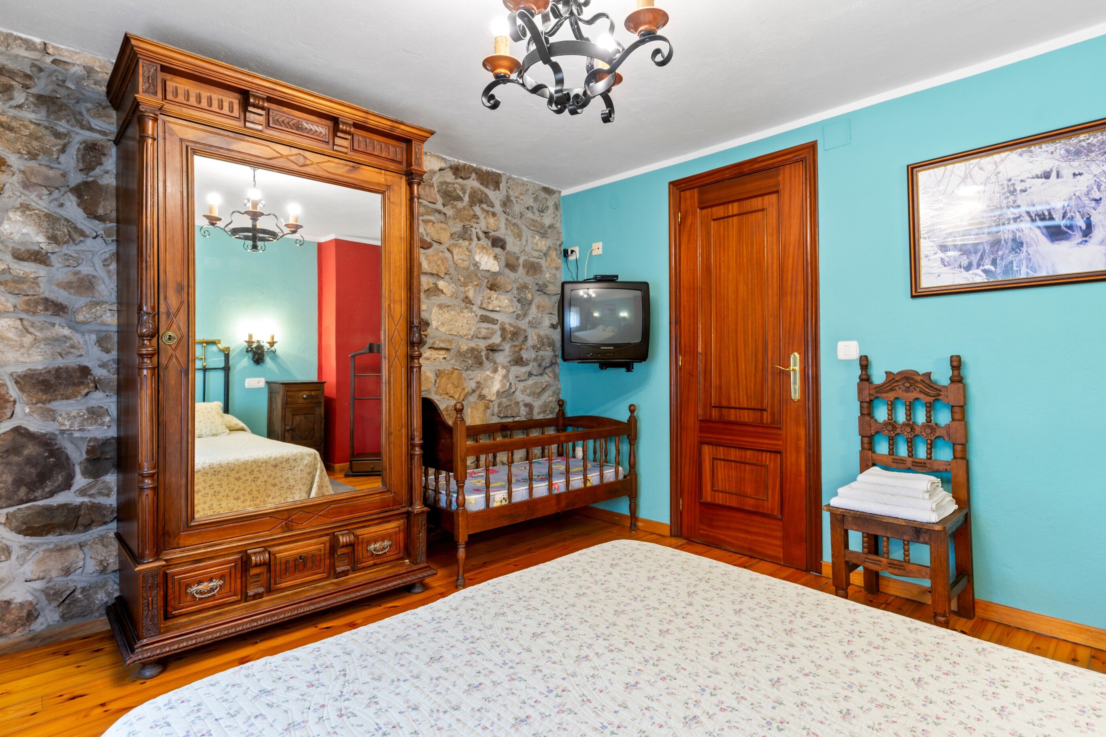 Una camera da letto con un ampio armadio in legno, una televisione, un muro in pietra e una sedia di legno.