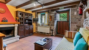 A rustic interior with a fireplace, wooden beams, stone walls, a sofa, and a television.