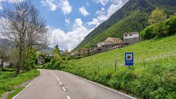 Eine Landstraße mit Häusern an einem Hang, ein Schild, das auf einen ländlichen Tourismusort hinweist, und ein klarer Himmel.