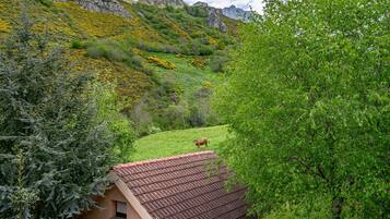A rustic building with a tiled roof, surrounded by lush greenery and a mountain backdrop.
