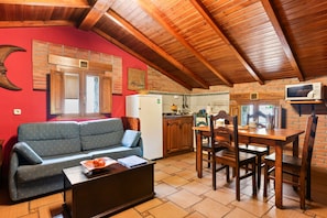 A cozy living area with a sofa, a dining table, and chairs, a kitchen with wooden cabinets, and a red wall with a crescent moon decoration.