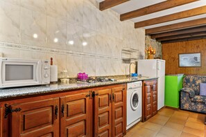 Une cuisine avec des meubles en bois, un four à micro-ondes, un lave-linge et un mur vert.