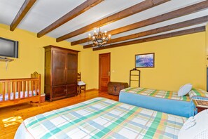 Une pièce avec des poutres en bois, un lustre, une télévision, une armoire, un lit recouvert d’une courtepointe à carreaux et un tableau accroché au mur.