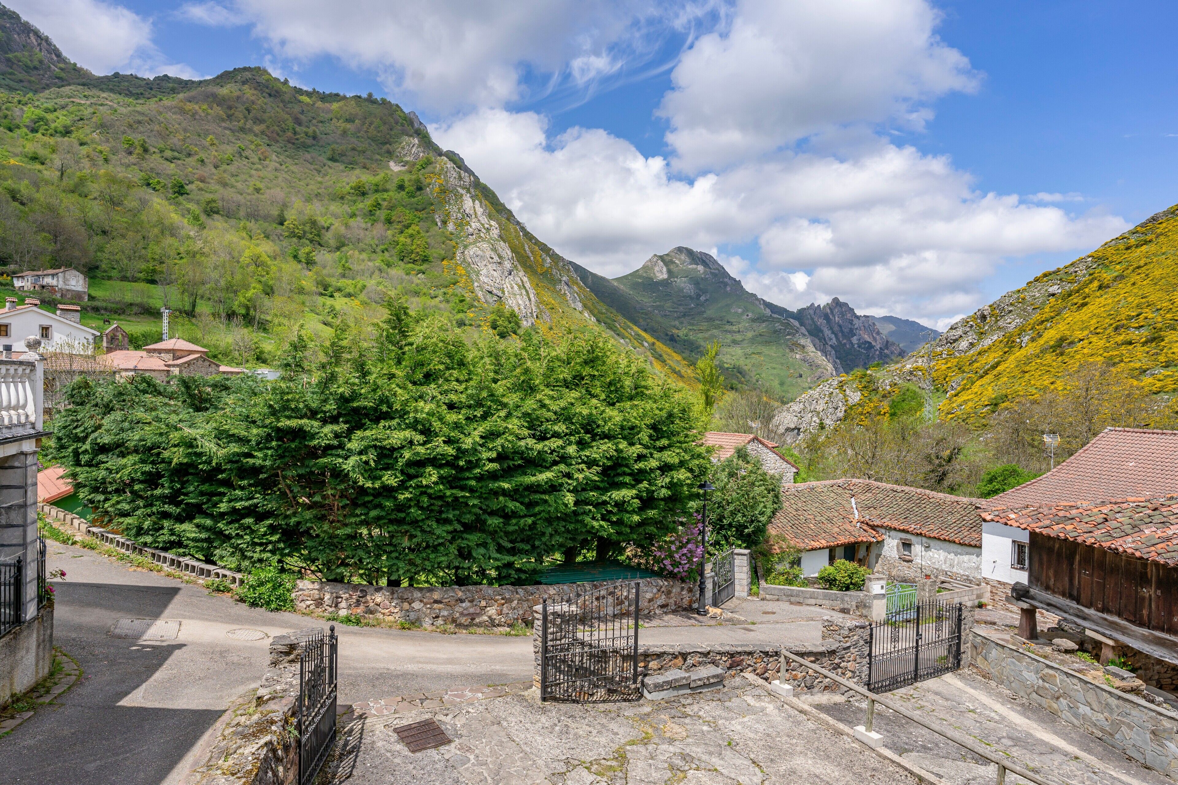 Un villaggio montano con edifici in pietra, una strada asfaltata e un cancello.