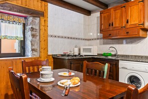 Una mesa de comedor de madera con sillas, una cocina con armarios de madera, un microondas y una lavadora.