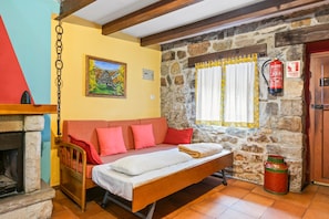 A cozy room with a bed, a sofa, a fireplace, a stone wall, and a window with curtains.