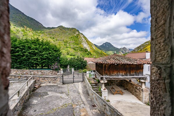 A stone courtyard with a wooden bench, a rustic building with a tiled roof, and a mountainous backdrop.