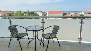 A balcony with two chairs and a table, overlooking a residential area with houses and a clear sky.