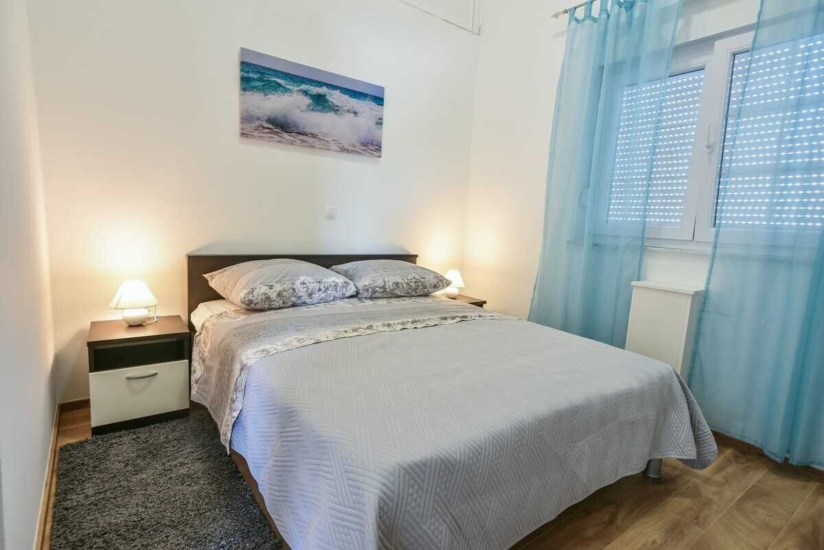 A neatly made bed with a patterned bedspread, a nightstand with a lamp, and a window with blinds.