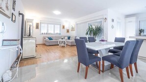 A modern living room with a sofa, a dining table with chairs, and a kitchen area with a refrigerator.