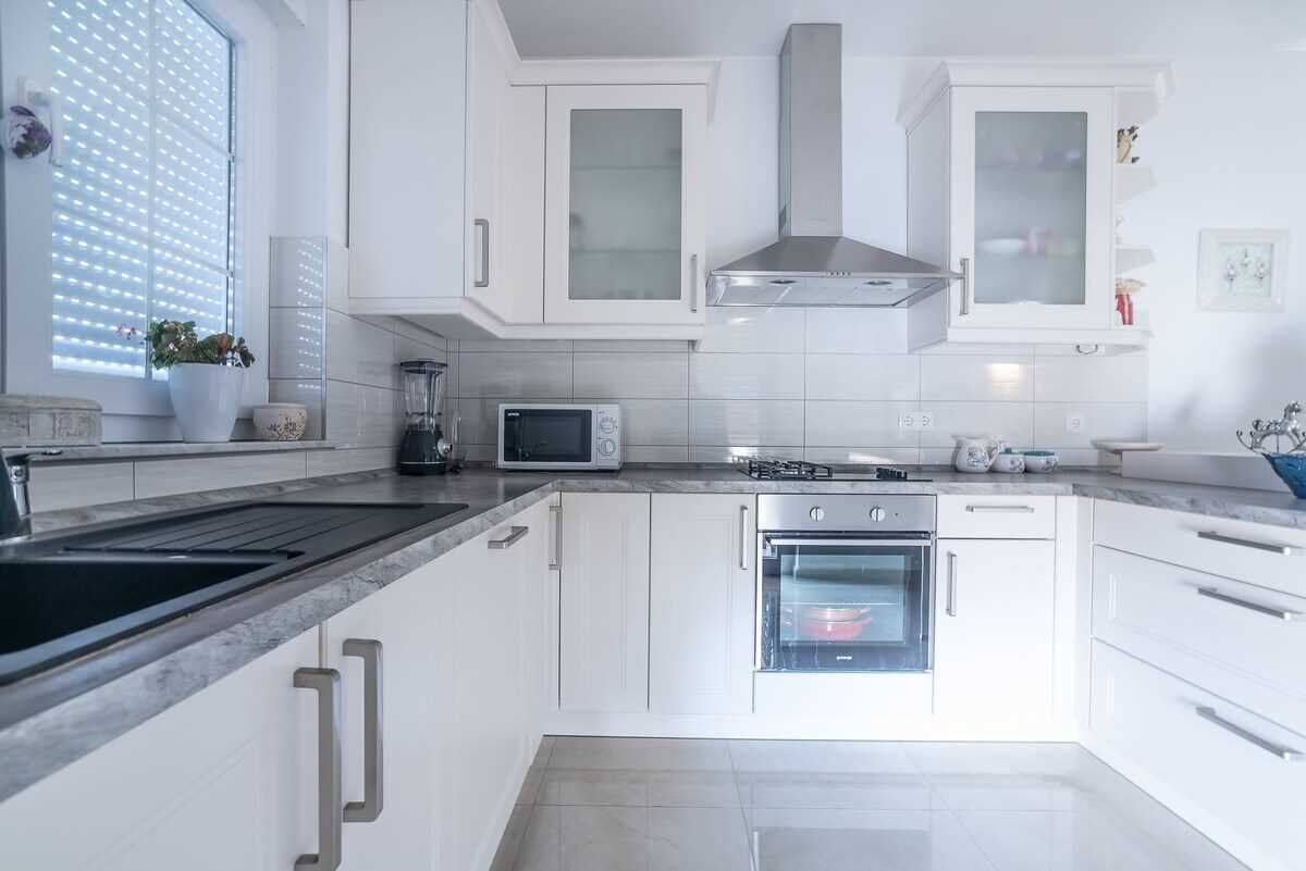 A modern kitchen with white cabinets, a built-in oven, a microwave, and a stainless steel range hood.