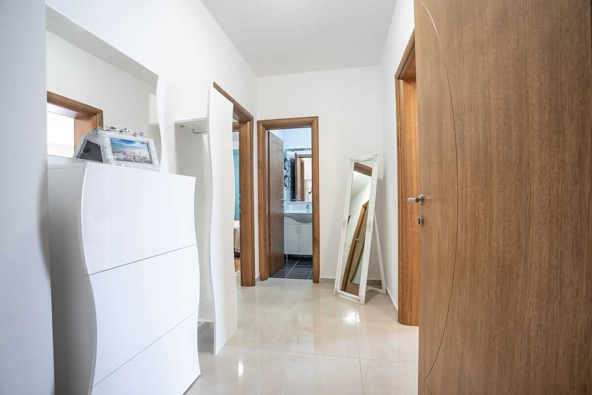 Um corredor estreito com um frigorífico branco, uma porta de madeira e um espelho encostado na parede.